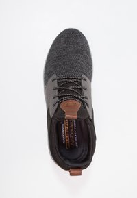 Scarpa sportiva nera con tomaia in maglia testurizzata, accenti grigi, dettaglio del tallone in pelle marrone, chiusura con lacci e soletta in schiuma memory.