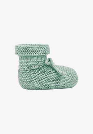 Chausson de bébé doux tricoté vert clair avec un revers et un nœud noué sur le côté, présenté sur fond blanc.