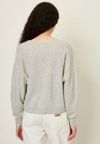 Pull gris clair en maille douce, avec une coupe ample, un col large et des manches longues, associé à un pantalon en denim blanc.