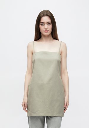 Haut caraco vert olive clair avec fines bretelles, un décolleté droit et un tissu texturé, porté avec un jean gris. Design simple et minimaliste.