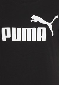 Musta puuvillainen T-paita, jossa on valkoinen "PUMA"-logo ja hyppäävän kissan kuvio oikeassa yläkulmassa, ja jossa on pyöreä pääntie.