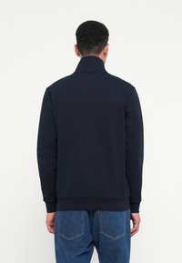 Donkerblauwe katoenen sweatshirt met een hoge kraag, lange mouwen en ribgebreide zoom. Achteraanzicht met een gladde textuur en minimalistisch ontwerp.