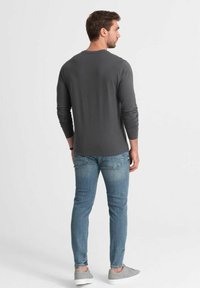 Langärmliges, graues Shirt aus weichem Stoff, kombiniert mit hellblauen Slim-Fit-Jeans und grauen Sneakers, zeigt ein einfaches, lässiges Design.