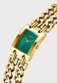 Gold-toned rectangular watch with a green dial and chain-link bracelet. Features a textured face and two hands. Brand logo positioned at 12 o'clock.