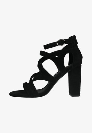 Sandale à talon haut en daim noir avec des brides entrecroisées et une boucle à la cheville. Talon carré et texture lisse.