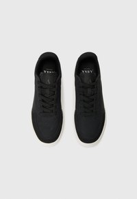 Black sneakers with a smooth synthetic upper, round toe, flat white rubber sole, and traditional lace-up closure. Minimal branding visible.