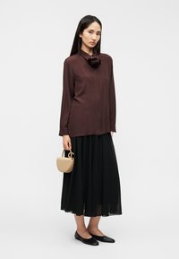 Μπορντό μπλούζα με υφή λουλουδιού στη γιακά, συνδυασμένη με μια ροή μαύρη φούστα και μια μικρή μπεζ τσάντα. Μαύρα επίπεδα παπούτσια.