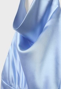 Tissu en satin bleu clair avec des plis lisses et une surface brillante et réfléchissante sur un fond clair uni.
