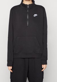 Svart zip-up fleece-tröja med hög krage, framficka i känguru-stil och vit Nike-logotyp på bröstet. Mjuk textur, avslappnad passform.