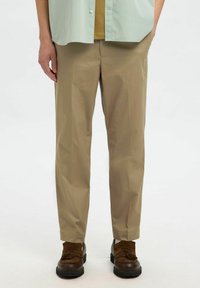 Beige rechte broek van gladde stof, met een strakke uitstraling en subtiele plooien, gecombineerd met bruine schoenen.