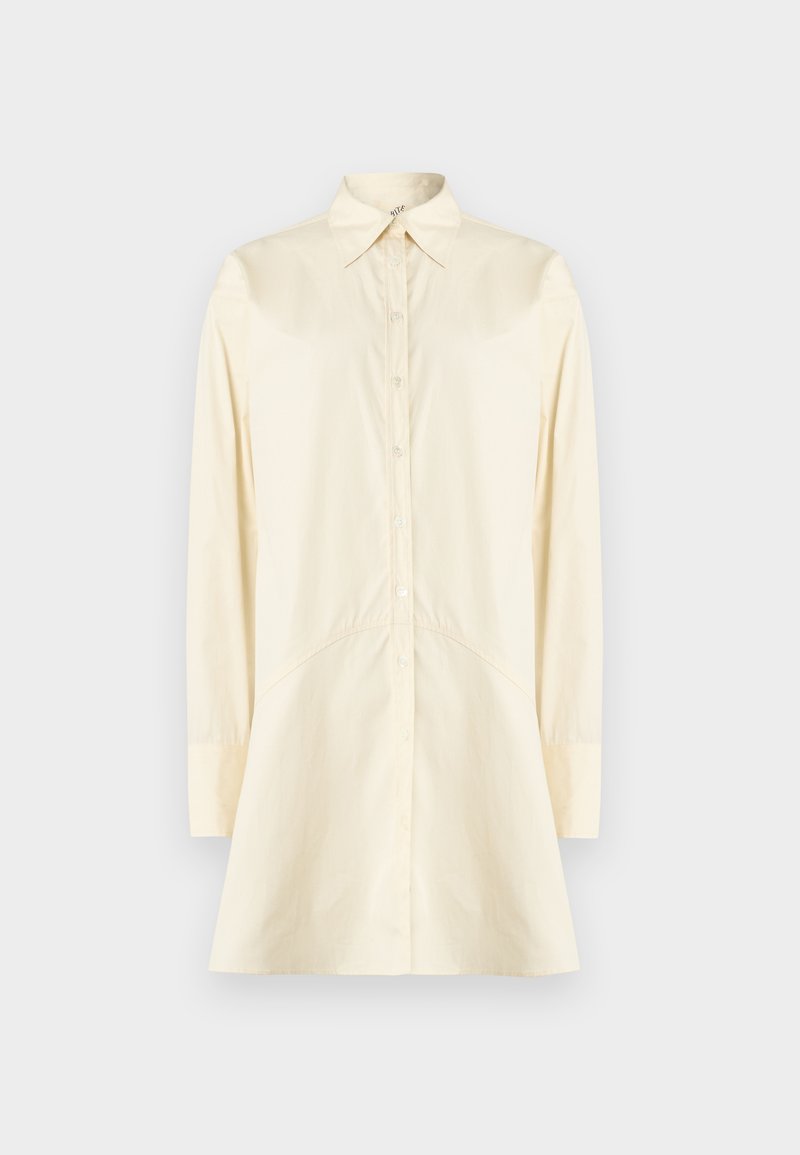 Chemise crème à boutons avec col pointu, manches longues et silhouette évasée ; fabriquée en tissu lisse, avec fermeture à boutons sur le devant.