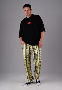 Black oversized t-shirt with a red logo, paired with yellow and black patterned loose-fit pants, and black sneakers.