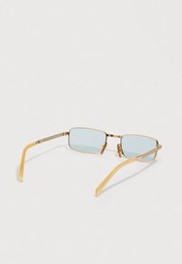 Pravokutne sunčane naočale sa svijetloplavim staklima i tankim zlatnim metalnim okvirom, odložene otvorene na bijeloj površini.