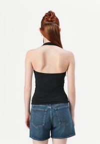 Top halter nero con una texture arricciata abbinato a pantaloni shorts di jeans blu a vita alta con tasche posteriori e orlo sfrangiato.