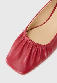 Chaussure plate en cuir rouge avec un bout carré arrondi et une texture froncée le long de l'ouverture, dotée d'un intérieur lisse beige.