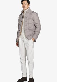 Grå quiltet puffjakke med høj krave, knaplukning og sidelommer, parret med en beige turtleneck og cremebukser.