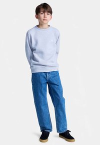 Sudadera gris claro con cuello redondo, combinada con vaqueros azules de corte holgado. Zapatos negros completan el look casual.