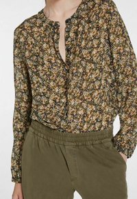 Blusa fluida de manga larga con un estampado floral oscuro en tonos de rosa, azul y verde; presenta un delantero con media botonera y cuello redondo, combinada con pantalones de cintura elástica en verde oliva.