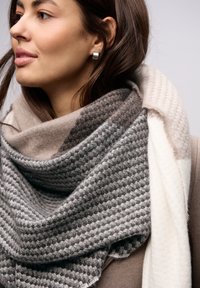 Geweven sjaal in tinten grijs en beige, met een gestructureerd patroon. Zacht materiaal dat om de nek valt, aangevuld met een lichte laag eronder.