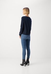 Tumesinise kudumisega sviiter pikkade varrukatega, koos helesiniste kitsaste teksade ja mustade kontsaga pahkluumudaga. Tagantvaade rõhutab lihtsat disaini.