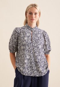 Blusa blu navy con motivo floreale bianco, maniche a sbuffo corte, scollo a chiave e tessuto morbido. Presenta una vestibilità rilassata e dettagli arricciati.