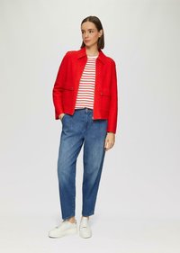 Rode wolmixjacket met een kraag, twee voorzakken, gedragen over een wit en rood gestreept shirt, gecombineerd met lichtblauwe jeans en witte sneakers.