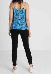 Blå leopardmönstrad camisole med tunna axelband, kombinerad med svarta skinny jeans och vita sneakers, sedd bakifrån.