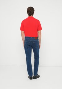 Punane lühikeste varrukatega polosärk, sinised sirge säärega teksapüksid tagataskutega, pruun nahast plaastriga vöörihm ning mustad kingad.