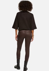 Pantalons marron ajustés avec des accents cloutés, associés à un haut noir surdimensionné avec des manches larges. Bottes noires épaisses aux pieds.
