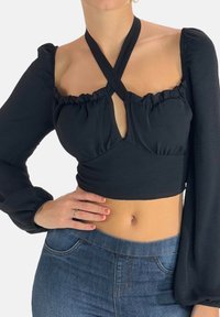 Zwarte cropped top met lange, opgepofte mouwen, ruches aan de halslijn en kruisbandjes. Heeft een sleutelgatuitsnijding en een zachte textuur.