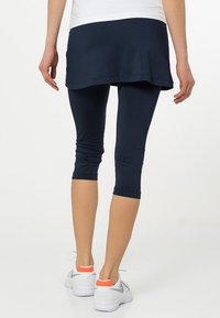 Falda deportiva azul marino sobre mallas capri a juego, mostrando una textura suave. Zapatillas blancas con detalles naranjas completan el conjunto.