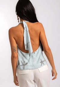 Haut halter bleu clair avec un dos nu, présentant des motifs floraux argentés. Fabriqué en tissu lisse, noué autour du cou avec un accent fluide.