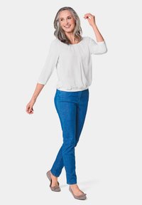 Weiße Bluse mit Dreiviertelärmeln und lockerer Passform, kombiniert mit blauen Slim-Fit-Jeans und grauen Ballerinas. Glatte Textur, lässiges Design.