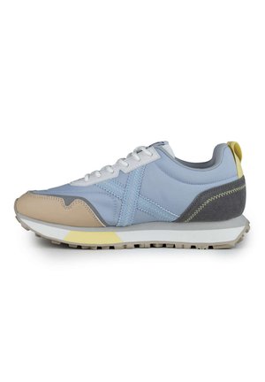 Zapatilla azul claro con acentos en beige y gris, cordones blancos, suela de goma, materiales texturizados y talón amarillo. Presenta detalles de costura.