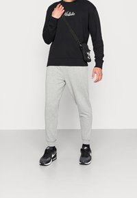 Černá mikina s logem "Hollister", šedé úzké tepláky a černé tenisky Nike; obsahuje nastavitelnou černou krosbody tašku.