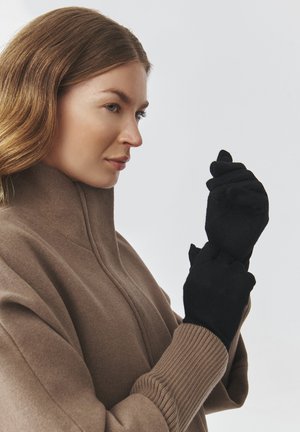 Guanti neri con una texture morbida, abbinati a un cappotto beige con colletto alto e polsini a costine. Il design è elegante e aderente.