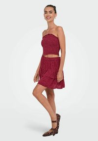 Bordeaux to-delt outfit med en strapless top med en bølget kant og en lagdelt nederdel. Tekstureret stof med blomstertryk. Brune nitterede sko.