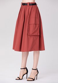 Une jupe midi couleur rouille en tissu léger, avec une taille élastique et une grande poche latérale, assortie à des talons noirs à lanières.