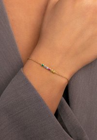 Pulsera de oro con cinco gemas de colores (verde, azul, púrpura, rosa, amarillo) engastadas en configuraciones circulares sobre una delicada cadena.