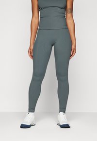 Szürke bordázott sportfelső és leggings szett, amely illeszkedő dizájnnal és varrás nélküli kivitelezéssel rendelkezik. Fehér sportcipők kék részletekkel teszik teljessé a megjelenést.