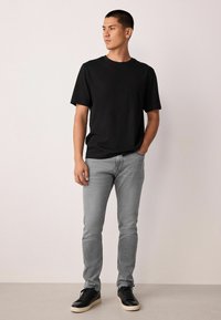 Fekete rövid ujjú póló, szürke slim fit farmernadrág és fekete sportcipő krémszínű talppal. Sima anyag és minimalista dizájn.