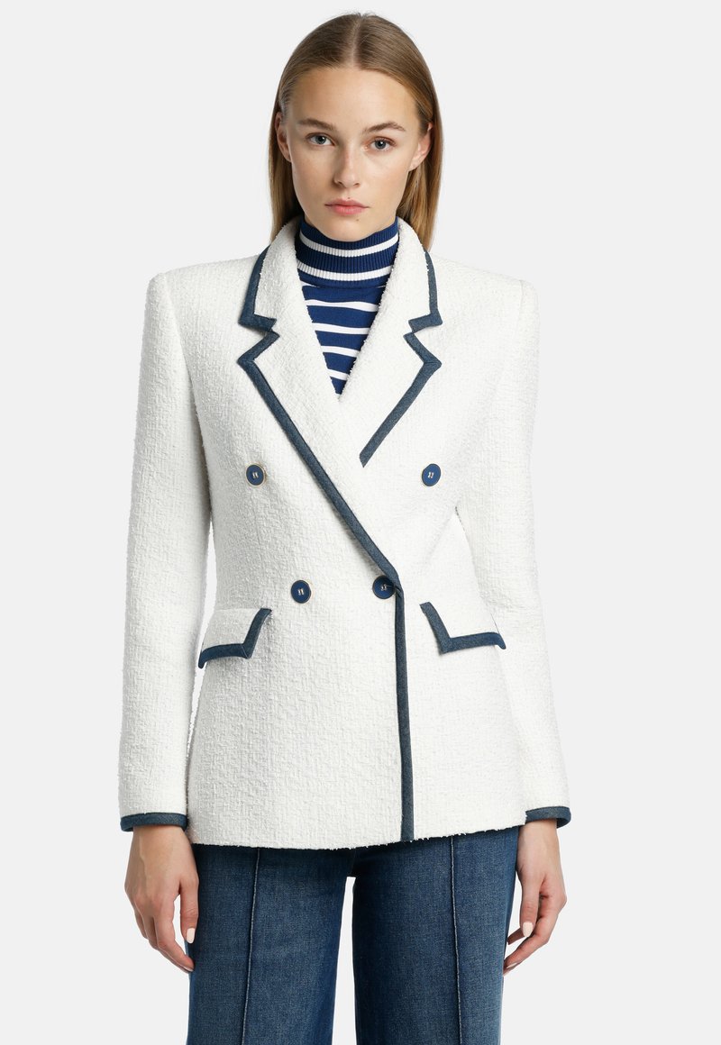 Witte textuur blazer met marineblauwe revers en knopen, met een dubbele sluiting aan de voorkant en twee voortassen. Draag over een gestreepte coltrui.