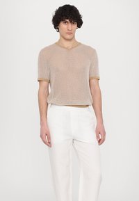 Haut en tricot beige à manches courtes avec texture côtelée et col contrastant marron clair, associé à un pantalon blanc ample.