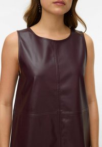 Vestido sin mangas color burdeos hecho de cuero brillante, con detalles de costuras y un cuello alto. Textura suave con un ajuste estructurado.