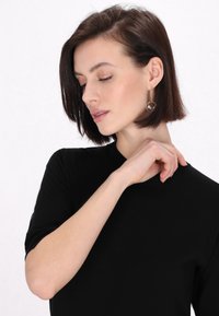 Top scurt negru cu mâneci scurte și decolteu rotund, textură netedă; model purtând cercei metalici lungi cu accente circulare.