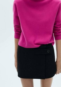 Pull en maille fuchsia avec col montant et manches longues, associé à une mini-jupe noire avec un détail de boutons sur le côté et un design à rabat.