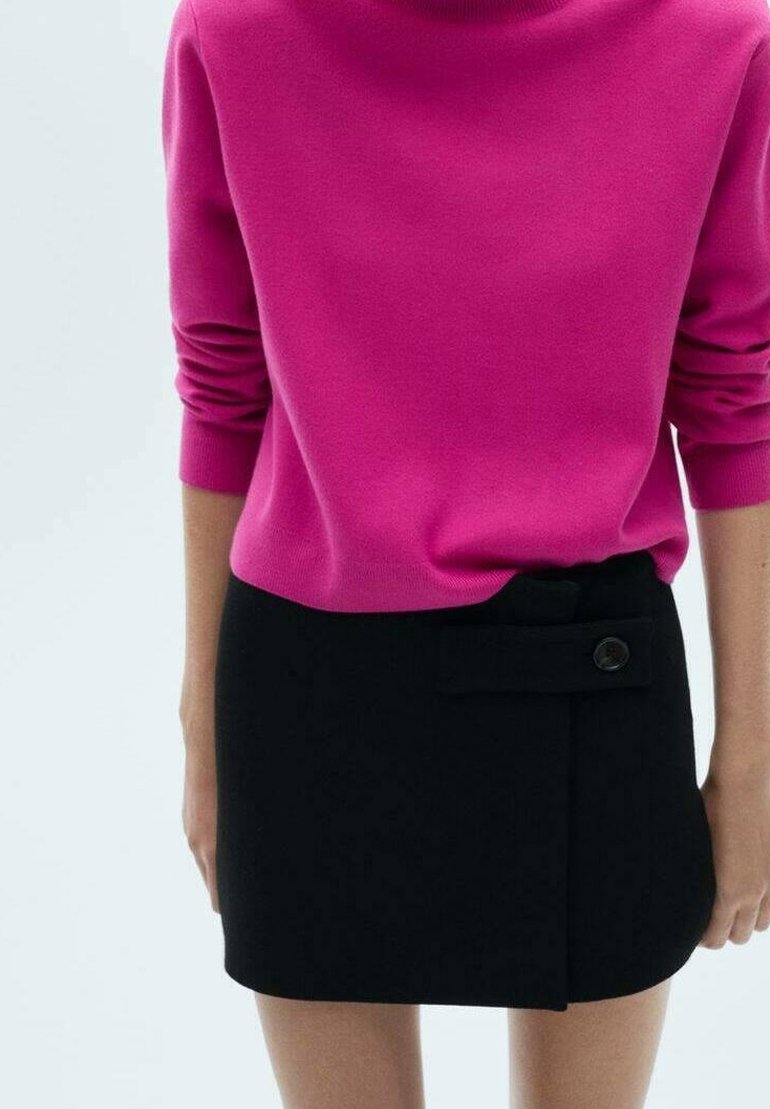 Pull en maille fuchsia avec col montant et manches longues, associé à une mini-jupe noire avec un détail de boutons sur le côté et un design à rabat.