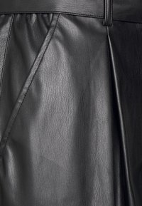 Pantalones de cuero negro con un acabado texturizado, diseño plisado y una cinturilla suave. Detalles cosidos a lo largo de las costuras.