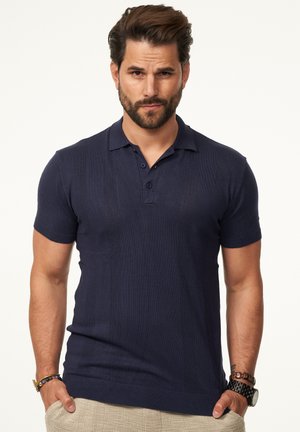 Navyblaues Kurzarm-Polo-Shirt mit strukturiertem Design, zwei Knöpfen und gerippten Bündchen. Getragen mit khakifarbenen Hosen.