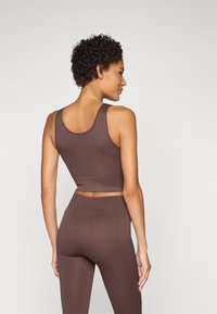 Brown ribbed crop top with wide straps, paired with matching high-waisted leggings. Smooth texture, fitted silhouette, and clean lines.